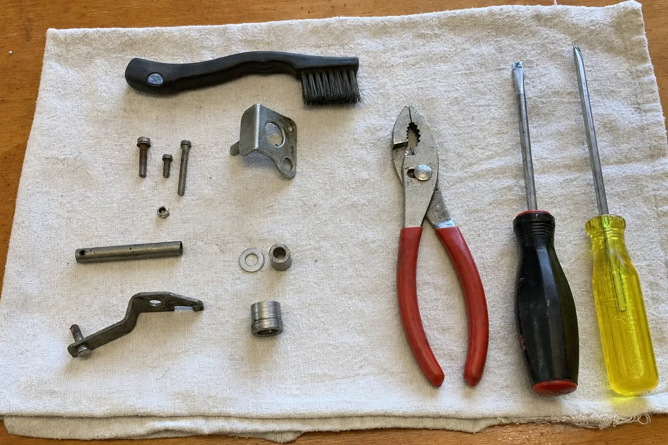 Hand tools on a cloth beside a latch lever, its pivot rod, a bushing and a threaded collar
